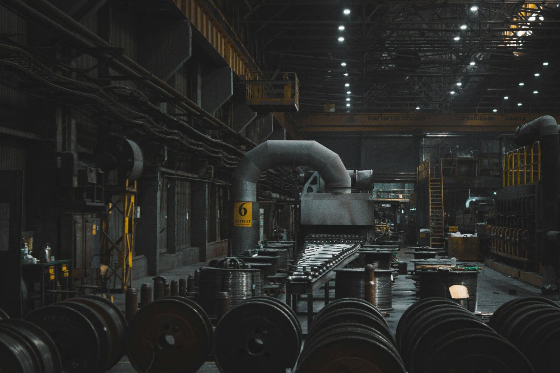 Interior of a heavy manufacturing plant with overhead cranes and rows of steel wire spools
